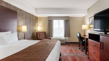 A hotel room with a large bed, a desk with a chair, a television, and two lamps.