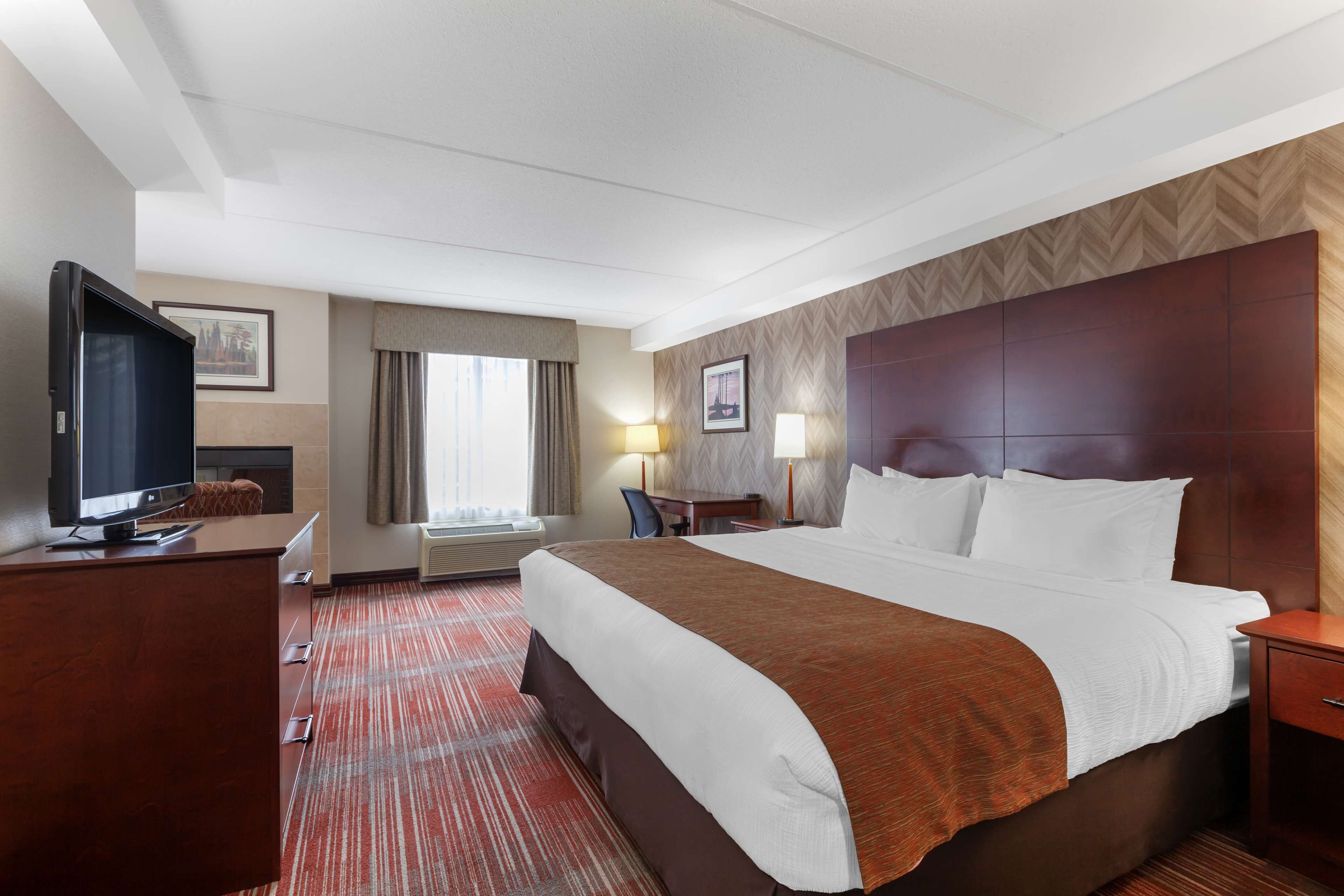 Une chambre d’hôtel avec un grand lit, un bureau doté d’un téléviseur à écran plat, une chaise, une lampe de bureau et une fenêtre avec des rideaux.