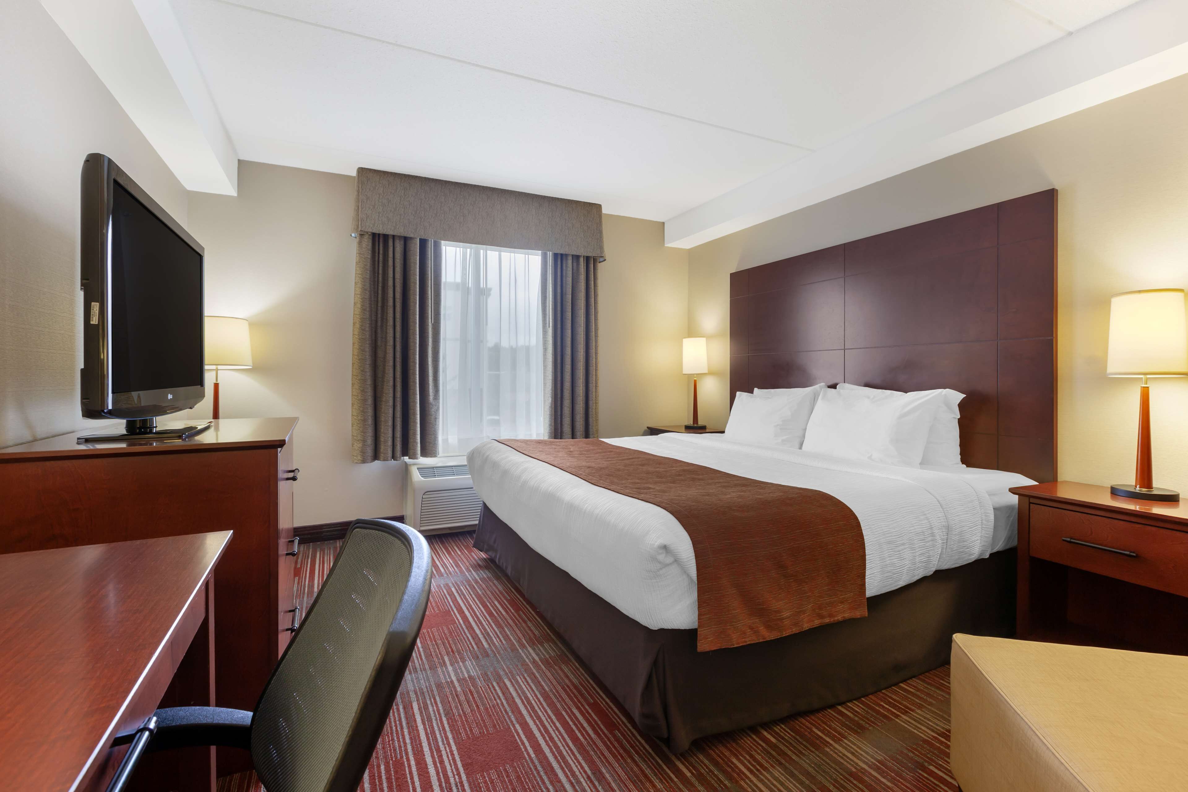 Une chambre d’hôtel équipée d’un lit, d’un bureau, d’une chaise, d’une télévision et de deux lampes de chevet.