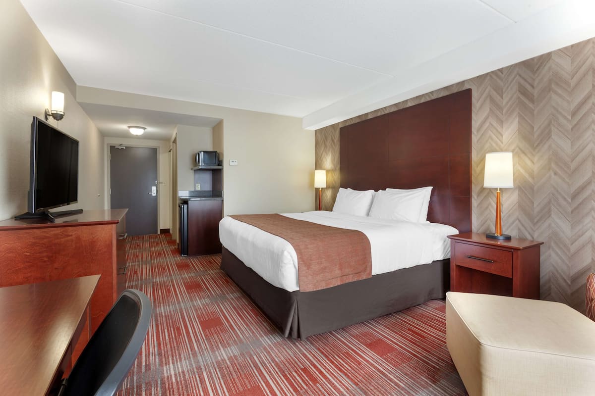 A hotel room with a bed, desk, TV, and a kitchenette.