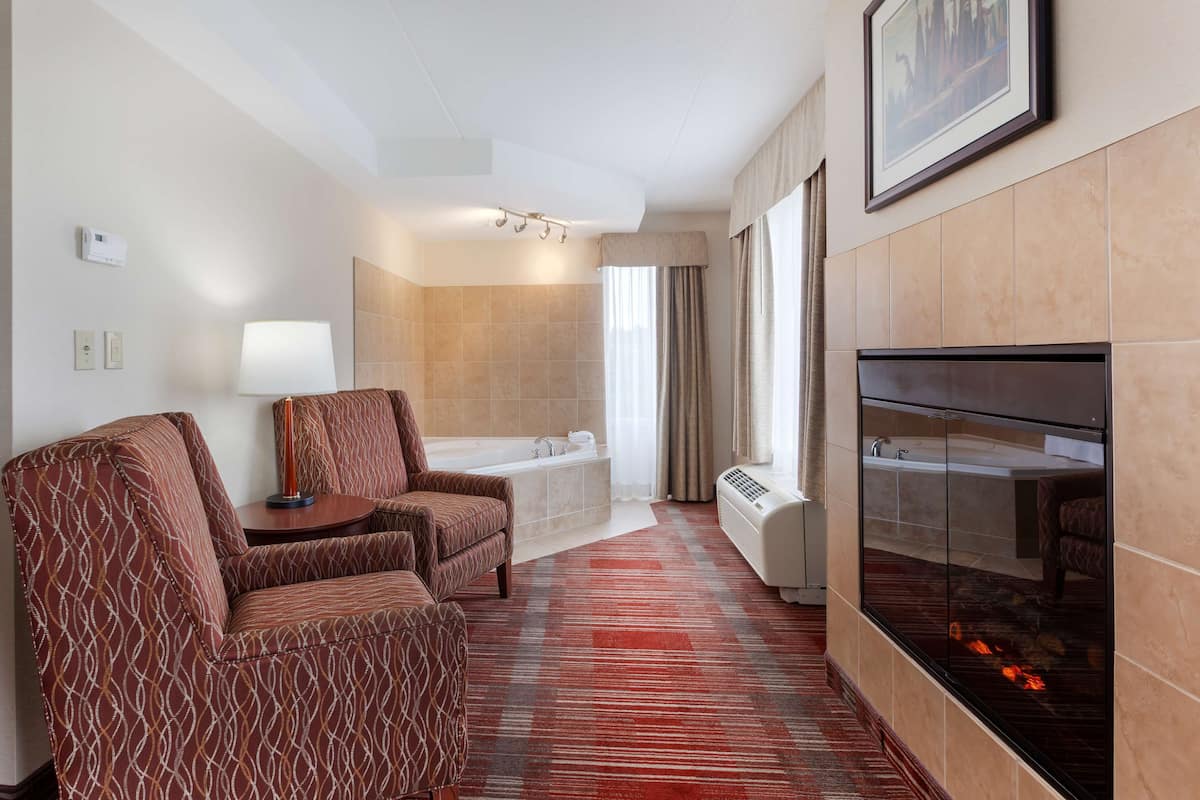 A hotel room with a fireplace, a bathtub, and two patterned armchairs.
