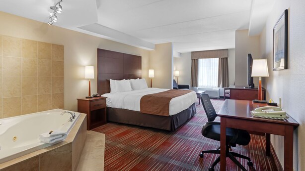 Ein Hotelzimmer mit einem großen Bett, einem Schreibtisch, einem Stuhl, einer Schreibtischlampe, einem Telefon und einem Badezimmer mit einer Badewanne.