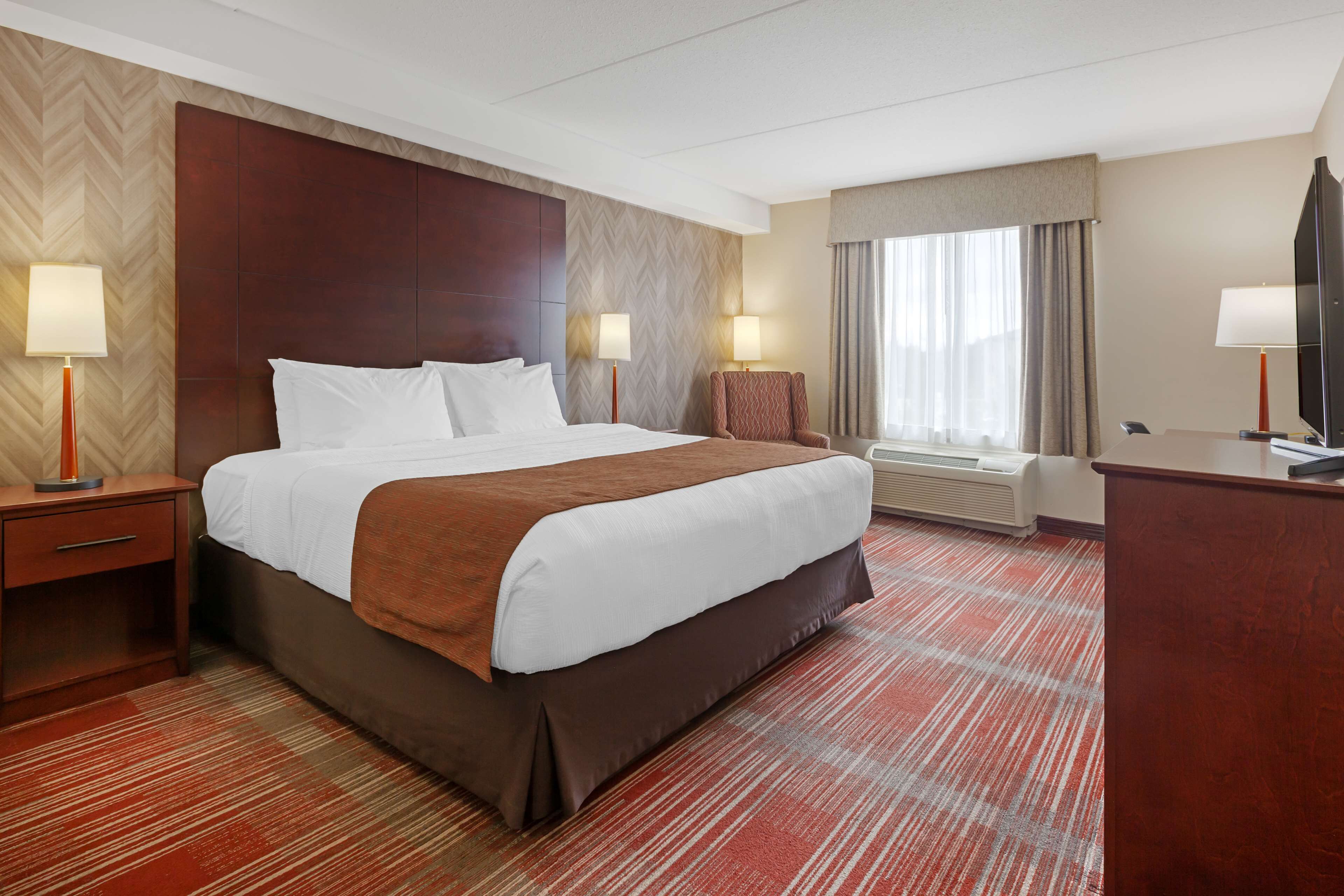 A hotel room with a large bed, two bedside lamps, a desk with a television, and a window with curtains.