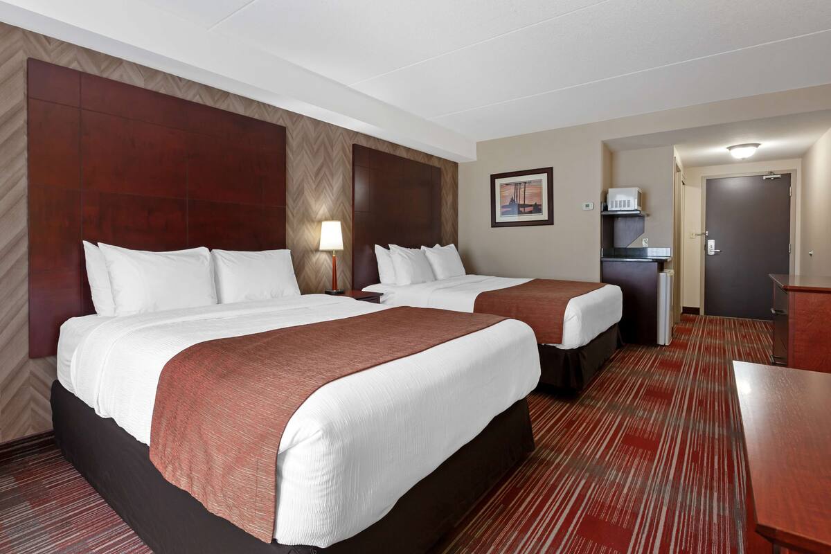 A hotel room with two beds, a desk, a lamp, a microwave, and a door.