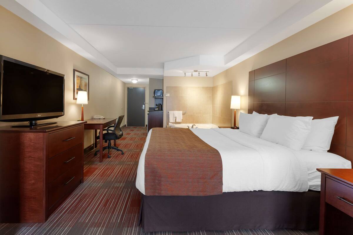 A hotel room with a large bed, a desk with a chair, a television, and a bathroom visible in the background.