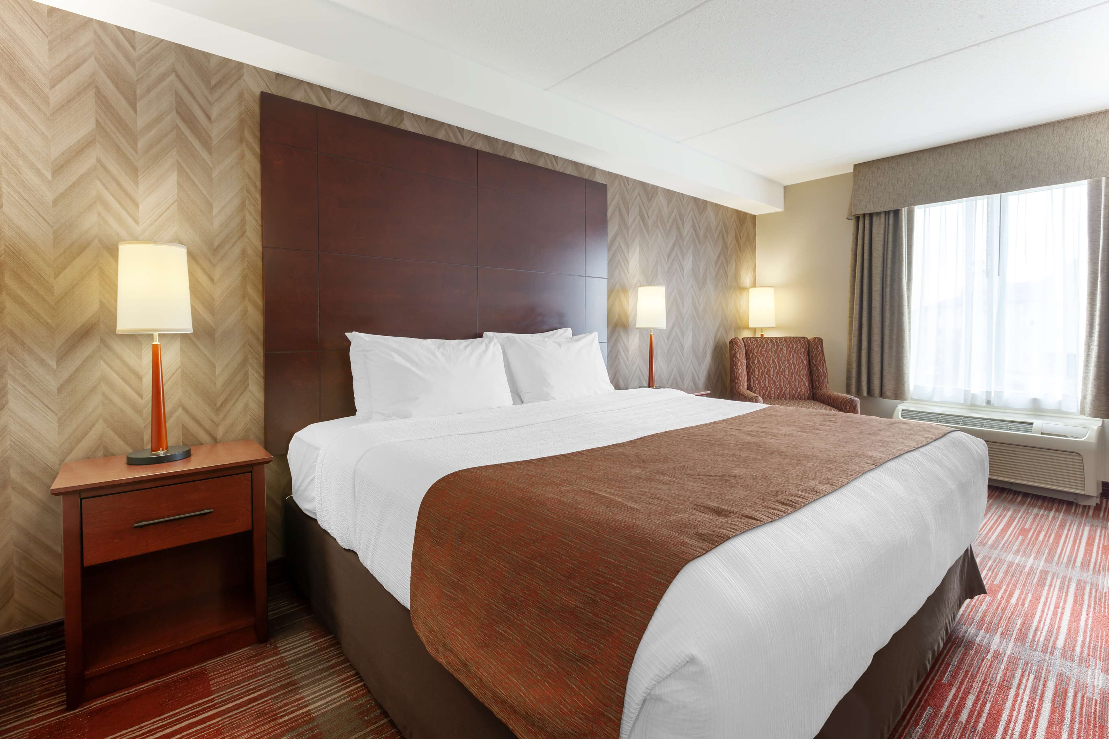 A hotel room with a large bed, two bedside tables with lamps, a chair, and a window with curtains.