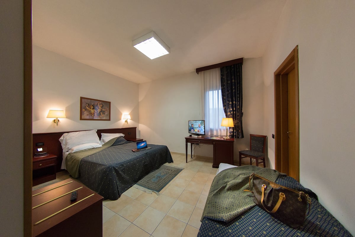A hotel room with two beds, a desk with a computer, a chair, and a lamp.