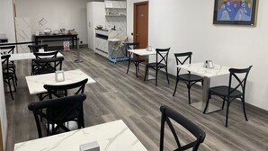 A dining area with tables and chairs, a kitchen area with marble countertops, and a door leading to another room. - Albergo Leonardo (Brescia)