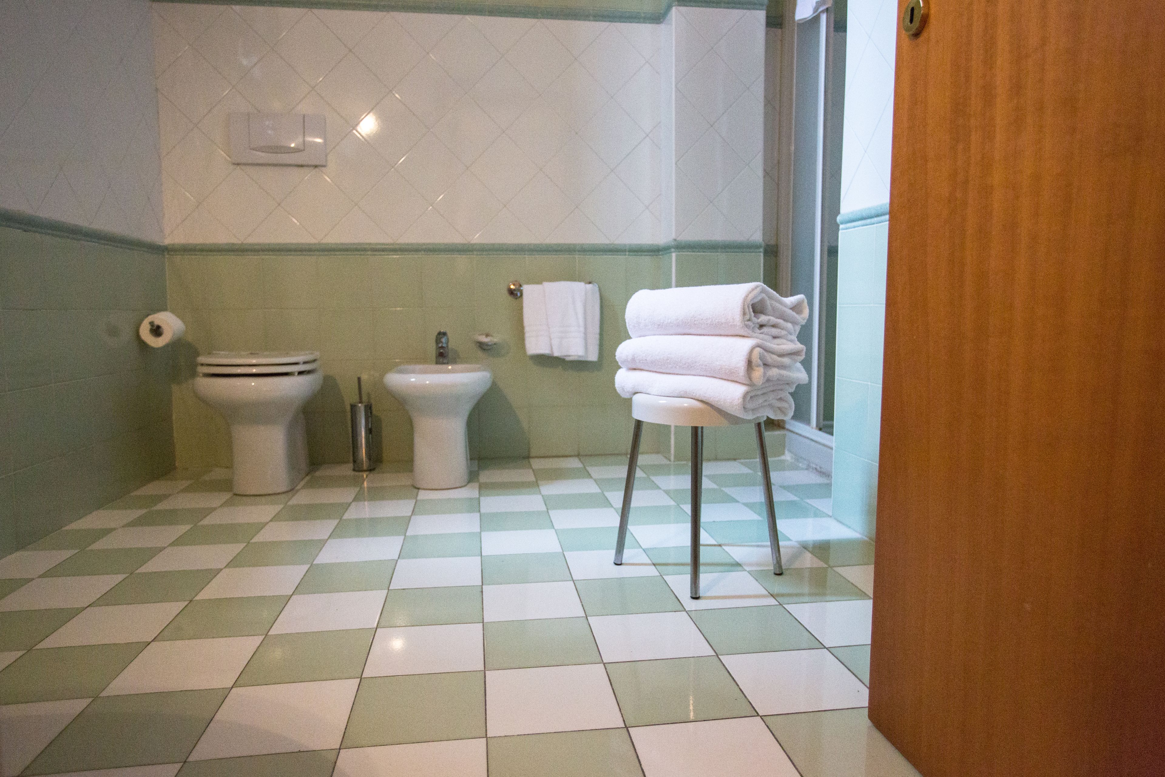 A bathroom with a checkered floor, a toilet, a bidet, and a stack of towels.