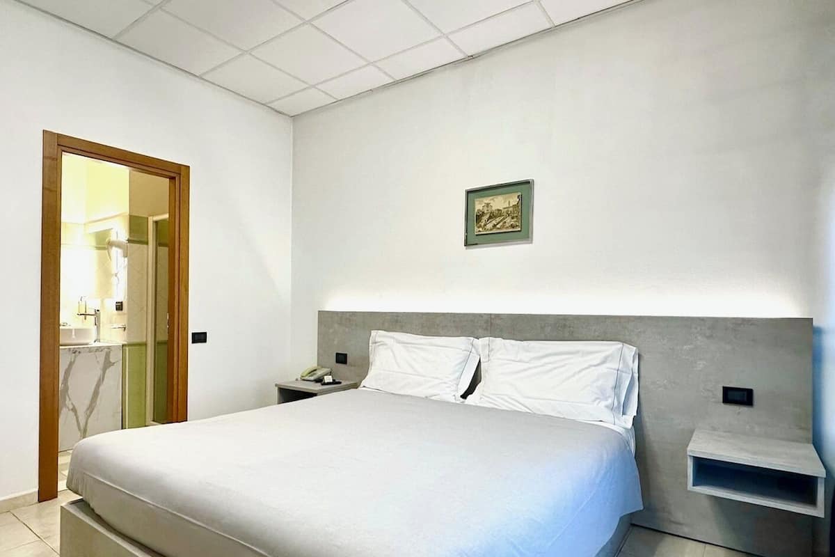 A bedroom with a large bed, a bedside table, a nightstand, and a framed picture on the wall.