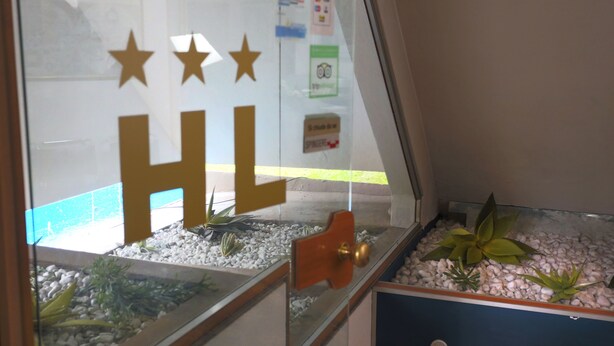A hotel reception area with a glass partition displaying the letters "HL" and three stars. - Albergo Leonardo (Brescia)