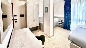 A hotel room with a bed, a desk, a wardrobe, a nightstand, and a window with curtains. - Albergo Leonardo (Brescia)
