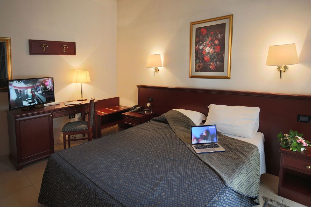A hotel room with a bed, desk, chair, TV, and two bedside lamps.