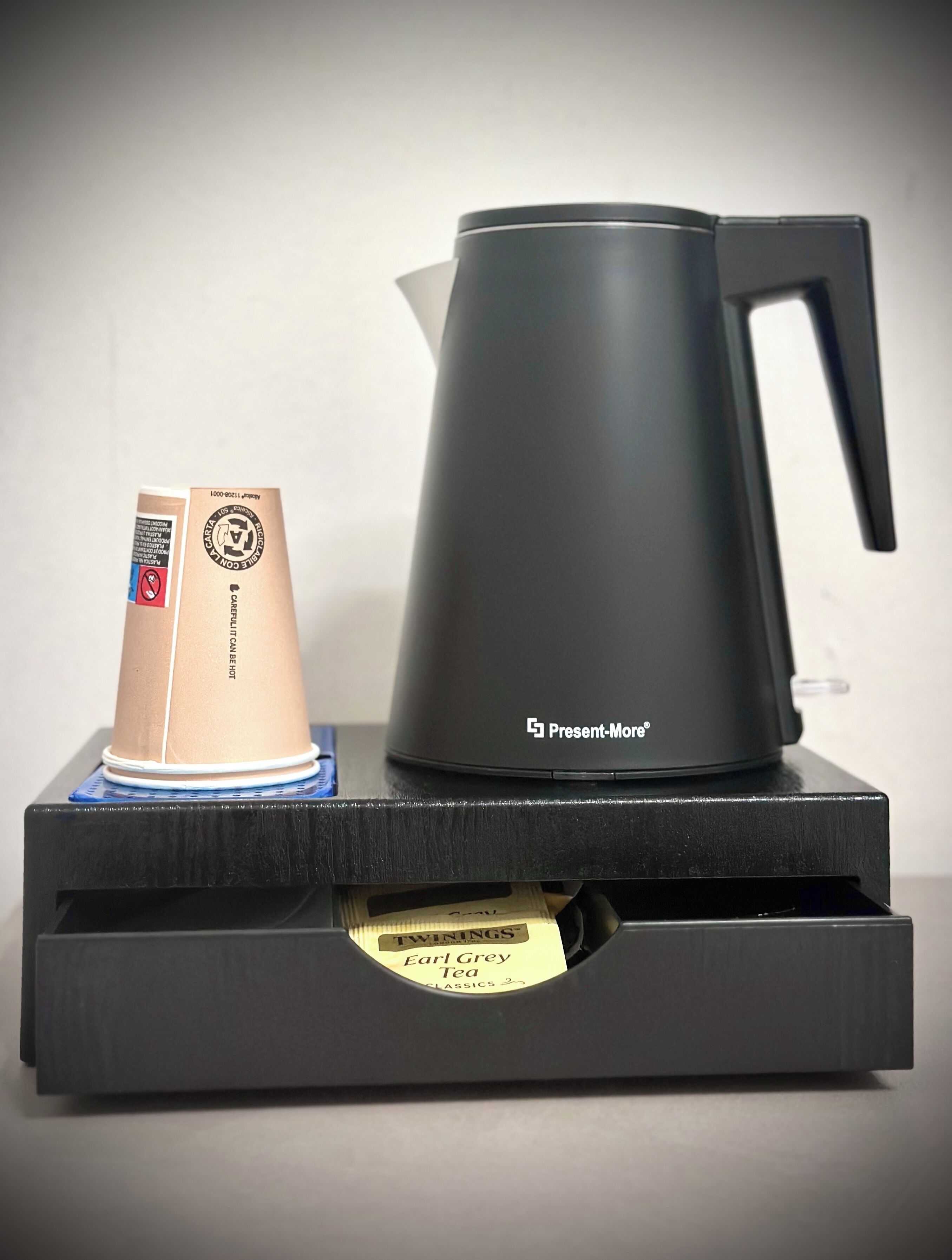 A black coffee maker with a handle on a black tray.