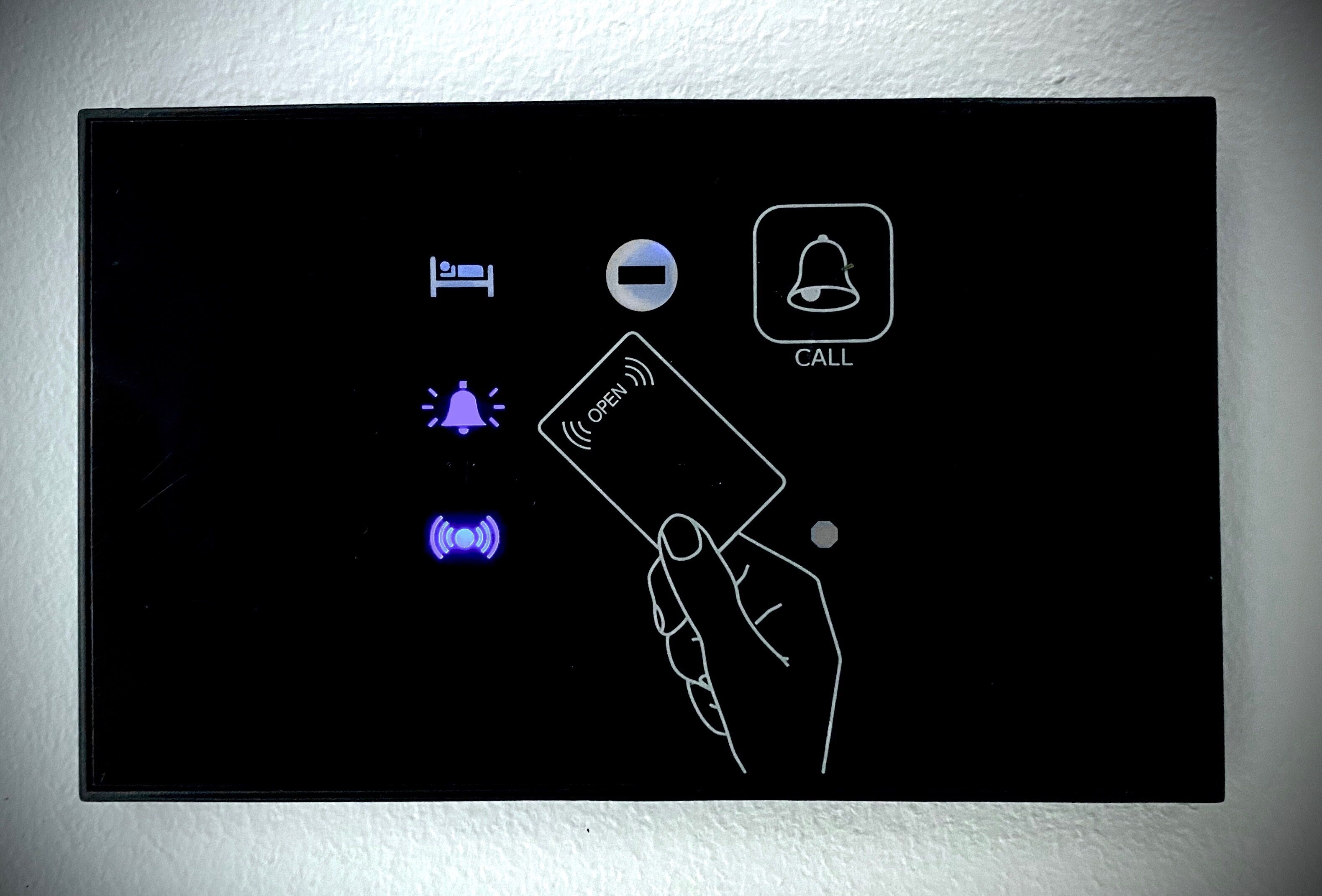 Panel de control con iconos para habitación, puerta abierta, llamada y una mano pulsando un botón.