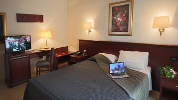Ein Hotelzimmer mit einem Bett, einem Schreibtisch mit Laptop, einem Fernseher und einem Nachttisch mit Lampe.
