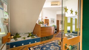 A reception area with a wooden desk, a blue patterned rug, and a small indoor garden. - Albergo Leonardo (Brescia)