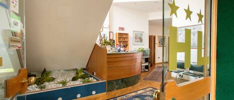A reception area with a wooden desk, a blue patterned rug, and a small indoor garden.