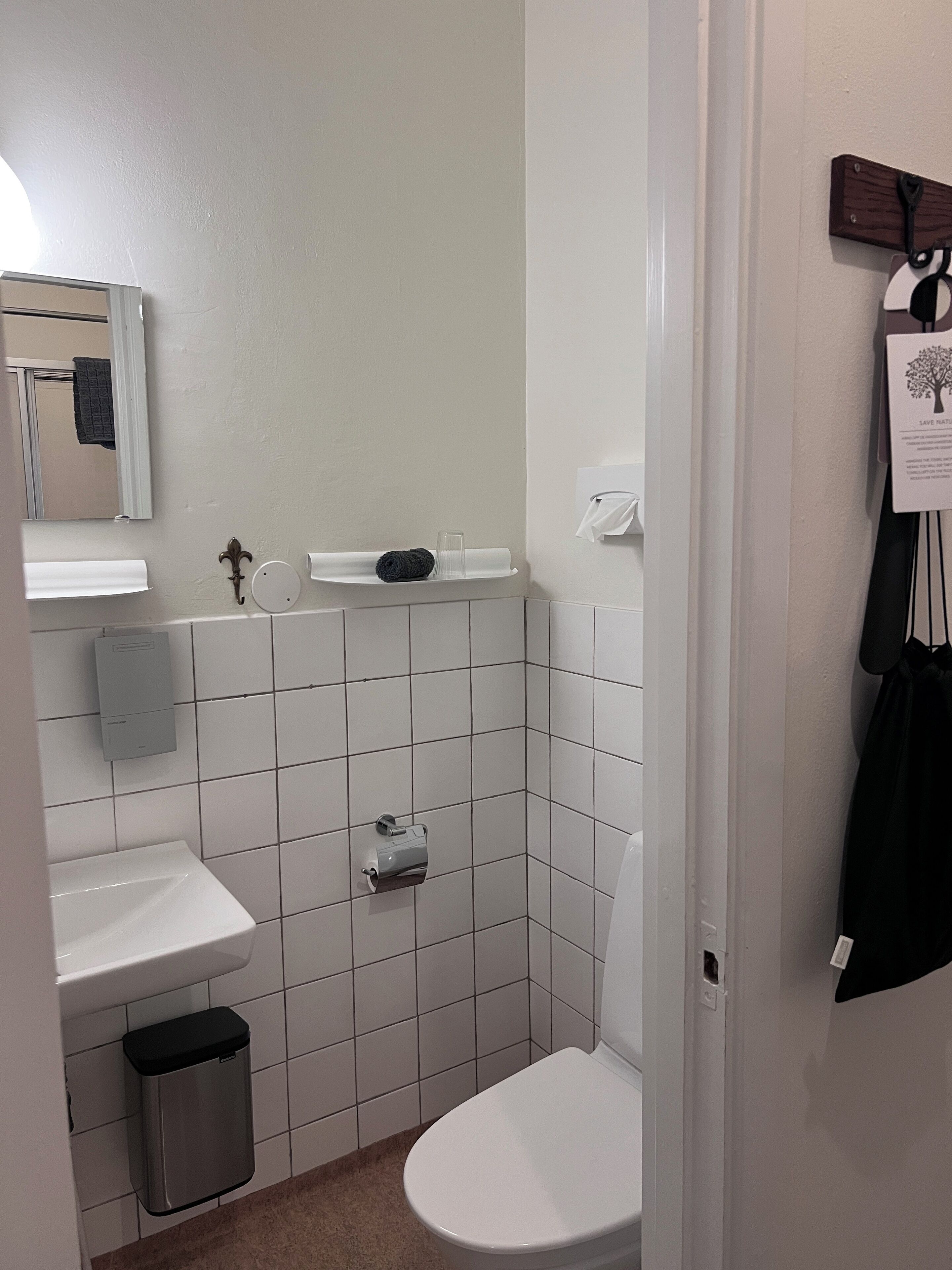 Ett litet, rent badrum med vita kakelplattor, en toalett, ett handfat och en spegel.