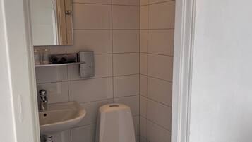 Un baño pequeño y limpio con azulejos blancos, un lavamanos, un inodoro y un espejo.