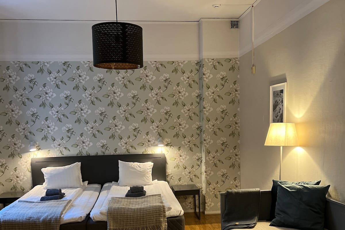 Quarto com uma cama de casal, mesa de cabeceira, abajur e uma mesinha.