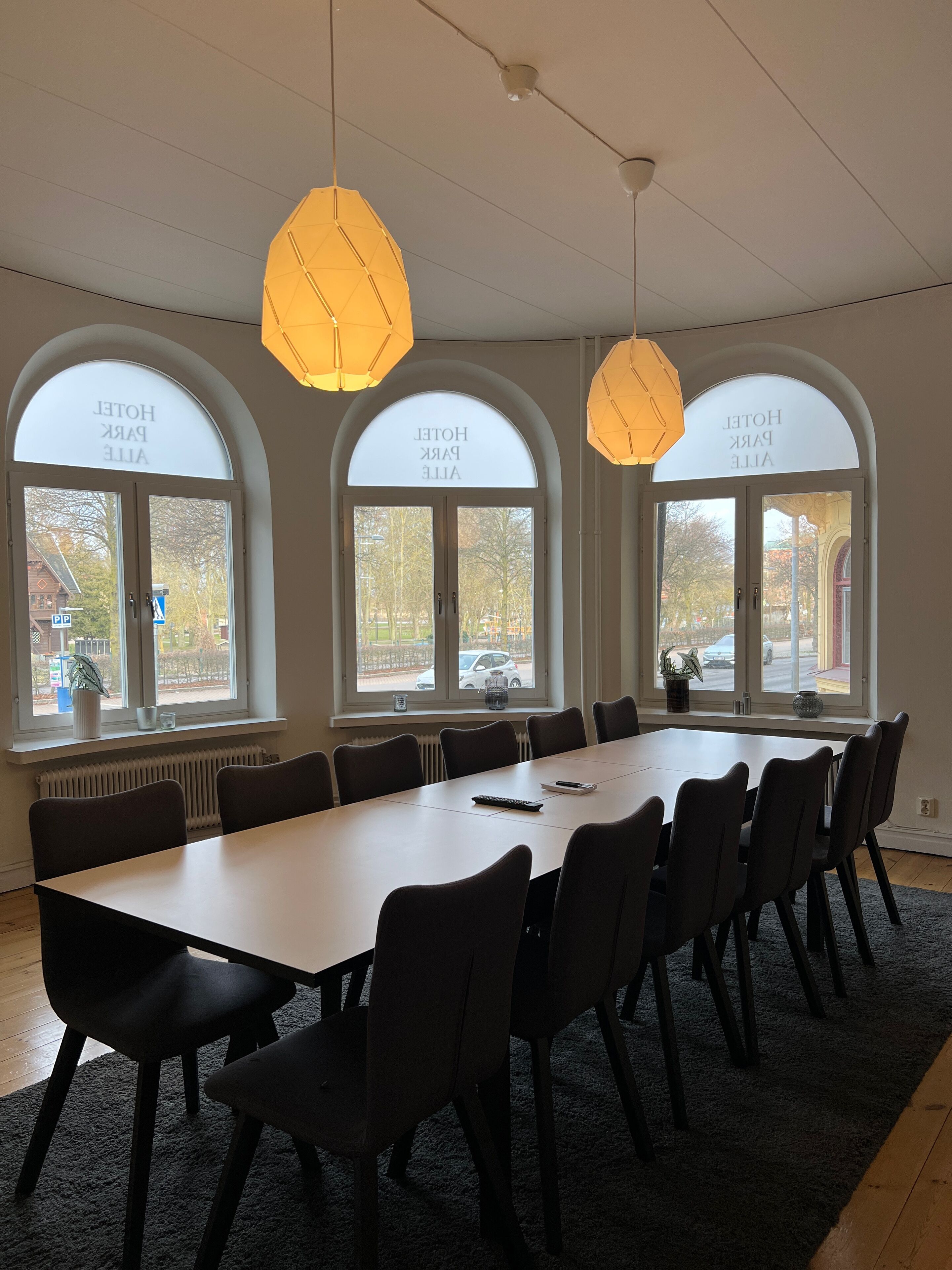 A conference room with a long table, multiple chairs, and large windows with arched tops.