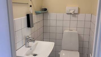 A small, modern bathroom with a white sink, a toilet, and a hand dryer.