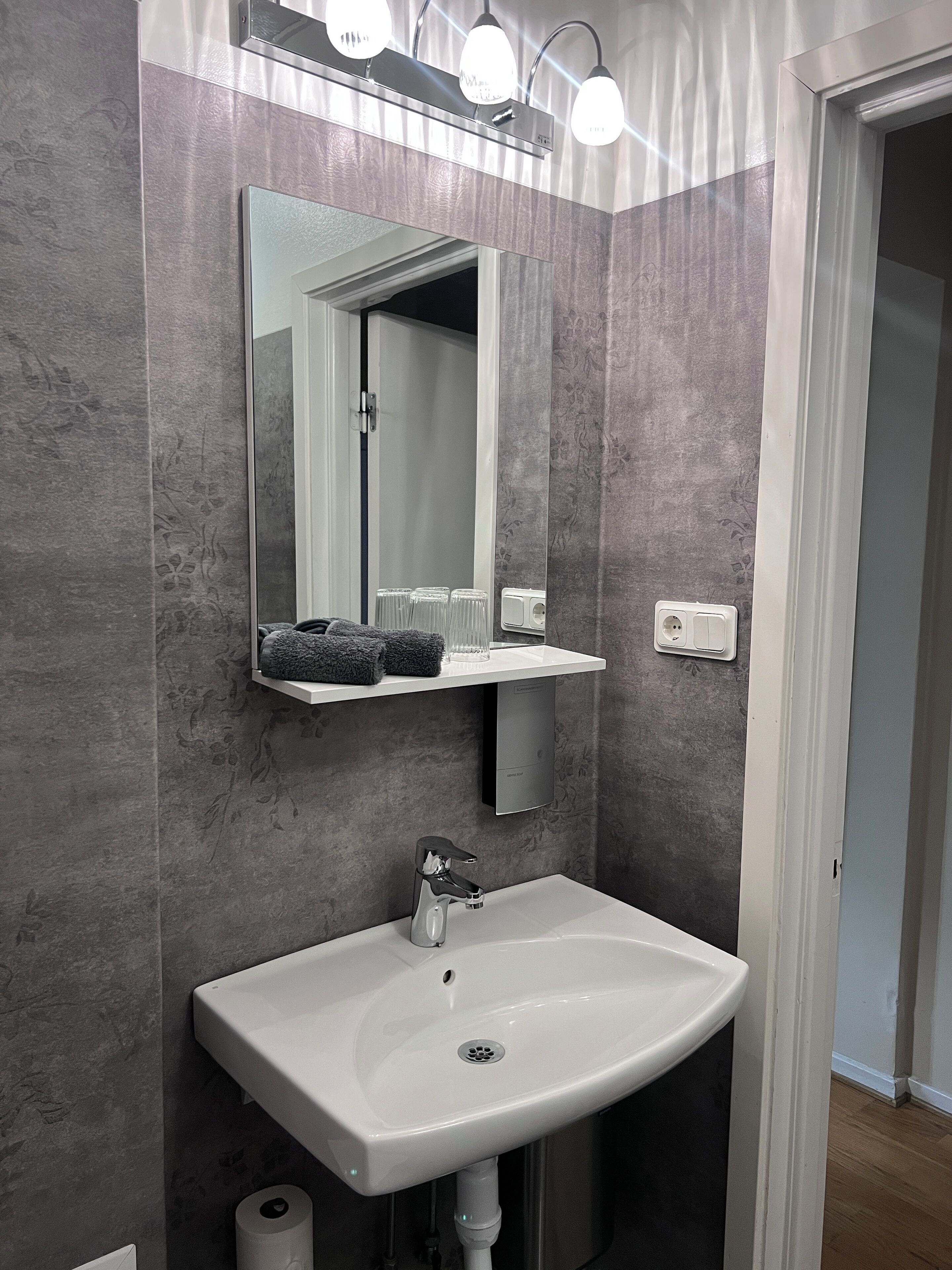 Un baño con lavamanos blanco, un espejo y un perchero para toallas.
