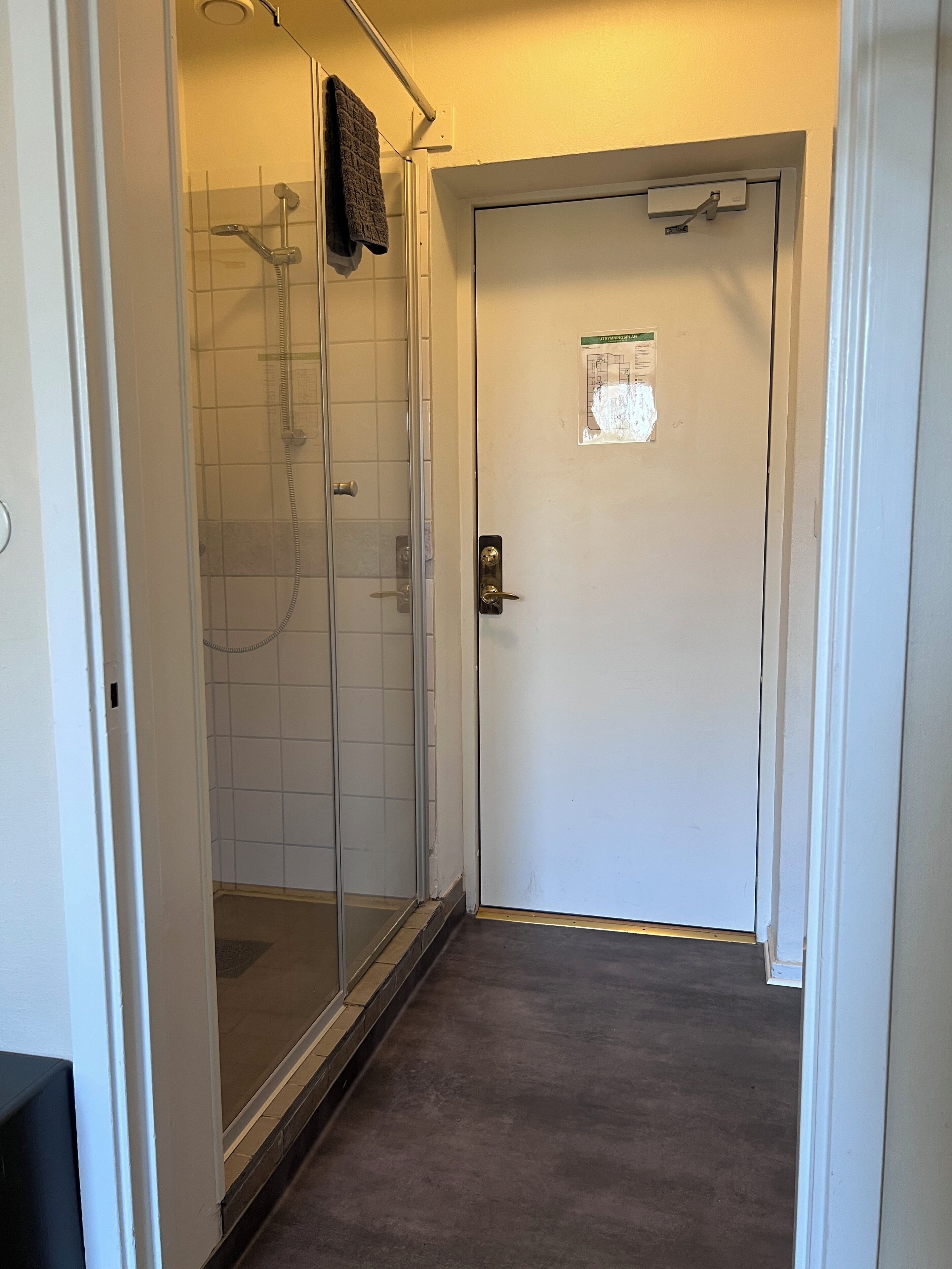 Ein Badezimmer mit Duschkabine aus Glas, einem Handtuch an der Wand und einer Tür mit kleinem Fenster.