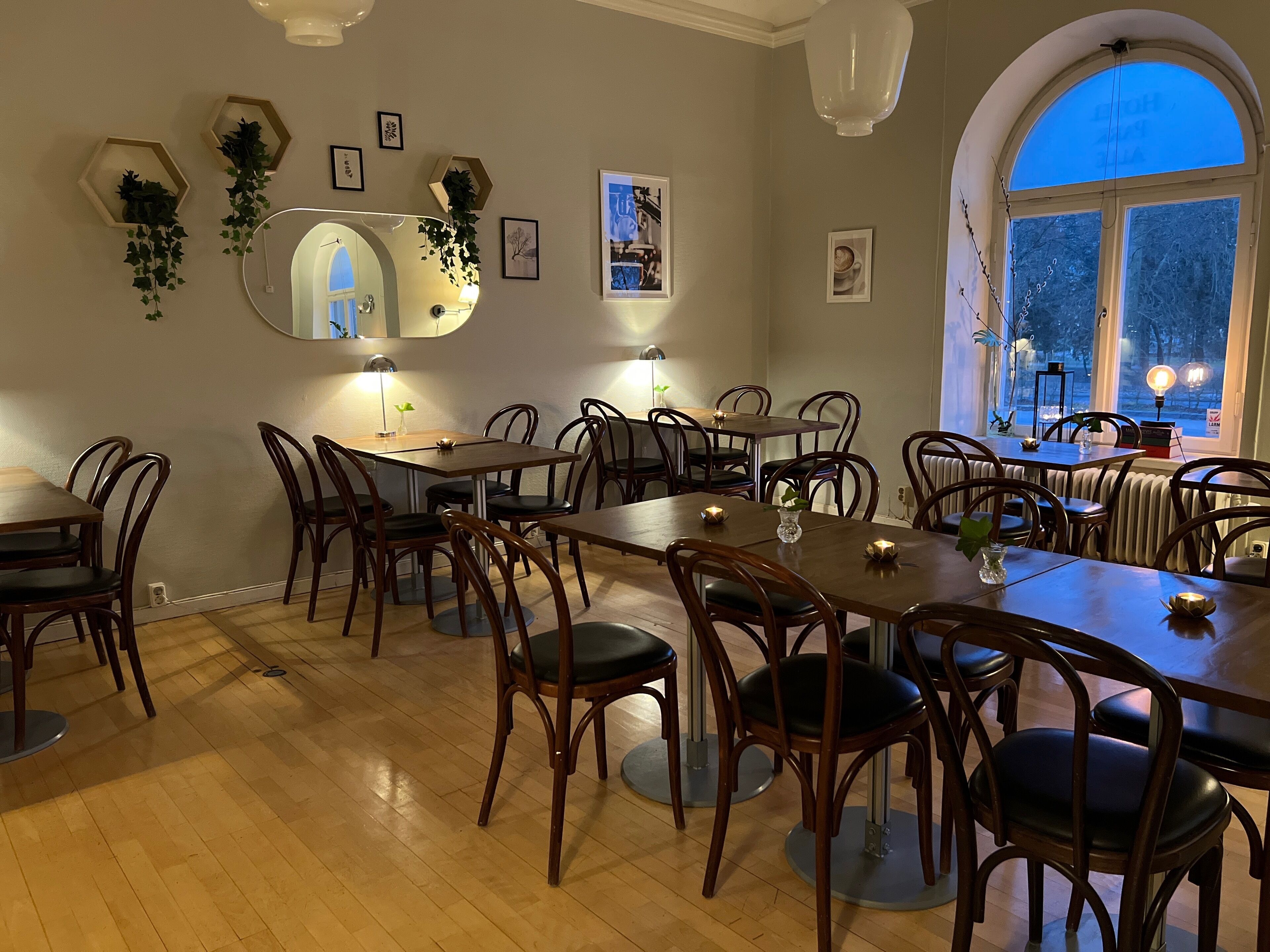 A dining area with wooden tables and chairs, a large mirror, and various wall decorations including framed pictures and plants.