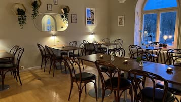 Un comedor con mesas y sillas de madera, un espejo grande y diversas decoraciones en las paredes, incluyendo cuadros y plantas.
