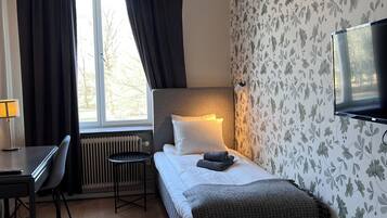 Habitación de hotel con cama, escritorio, silla, televisor y ventana con cortinas.