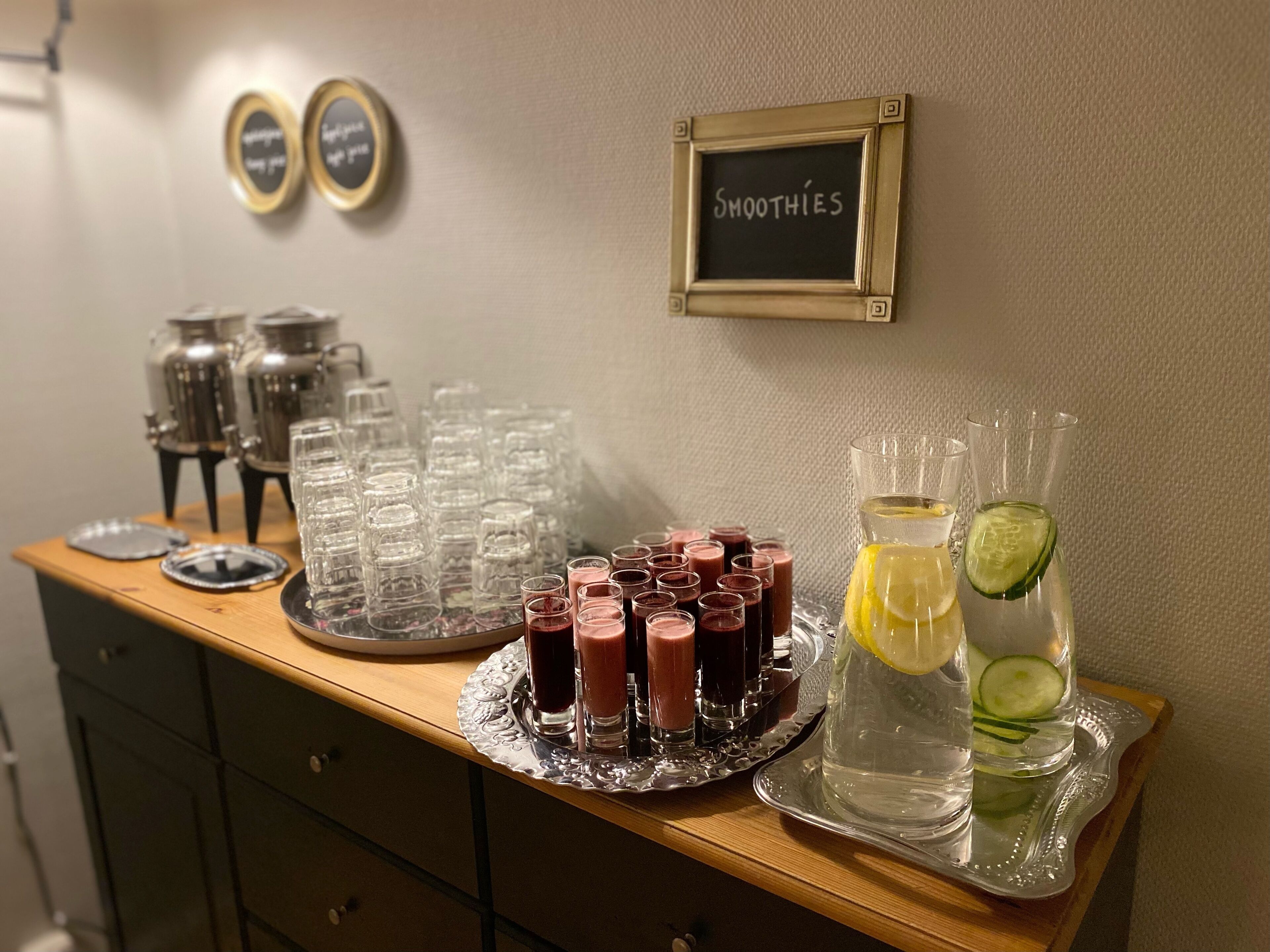 En bardisk med en tavla där det står "SMOOTHIES", ett bricka med små glas och en kanna med en citronskiva och gurka.