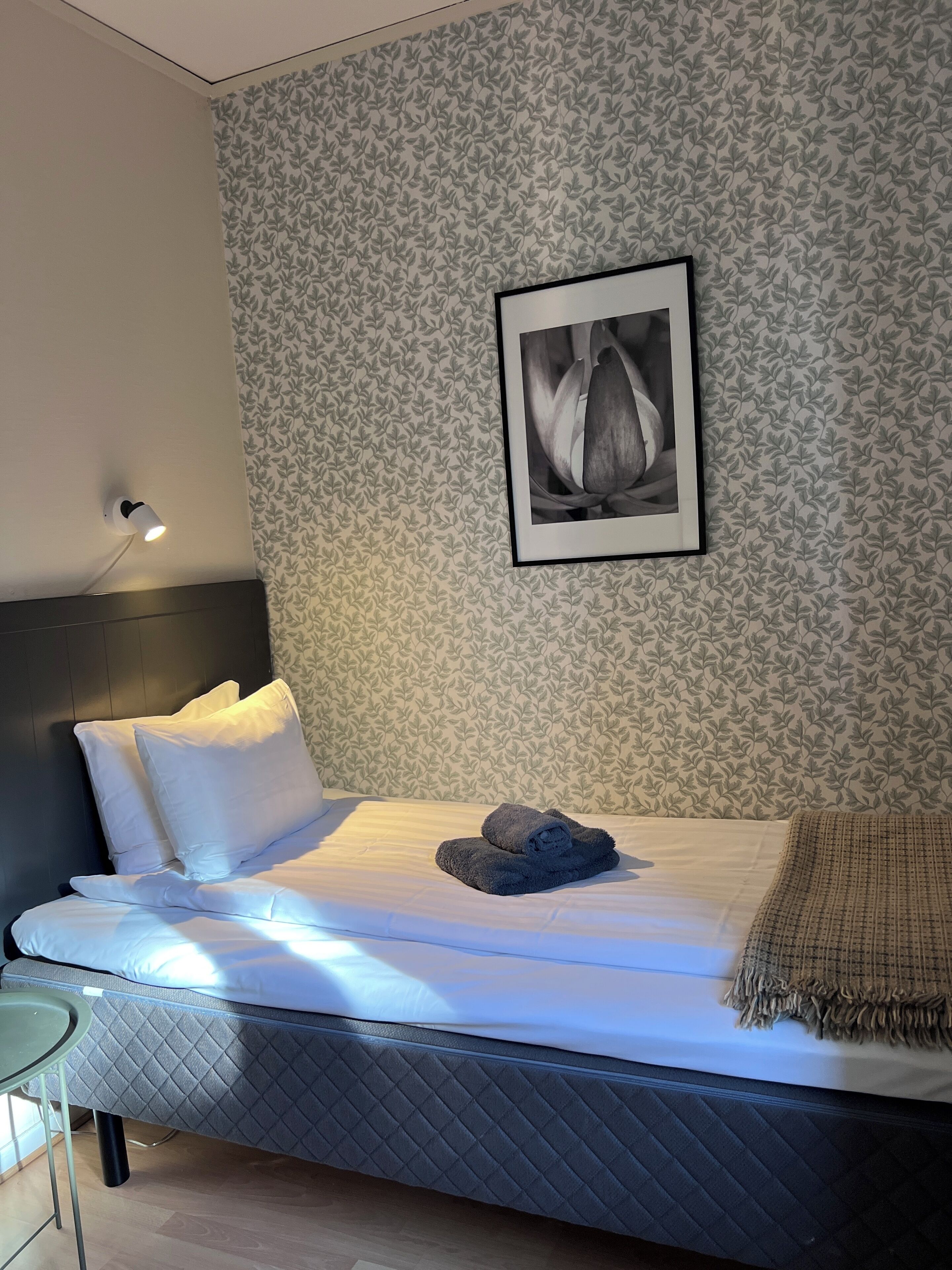 A neatly made bed with white linens, a dark headboard, and a patterned wallpaper.