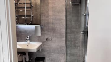 A modern bathroom with a glass shower enclosure, a sink with a mirror, and patterned floor tiles.