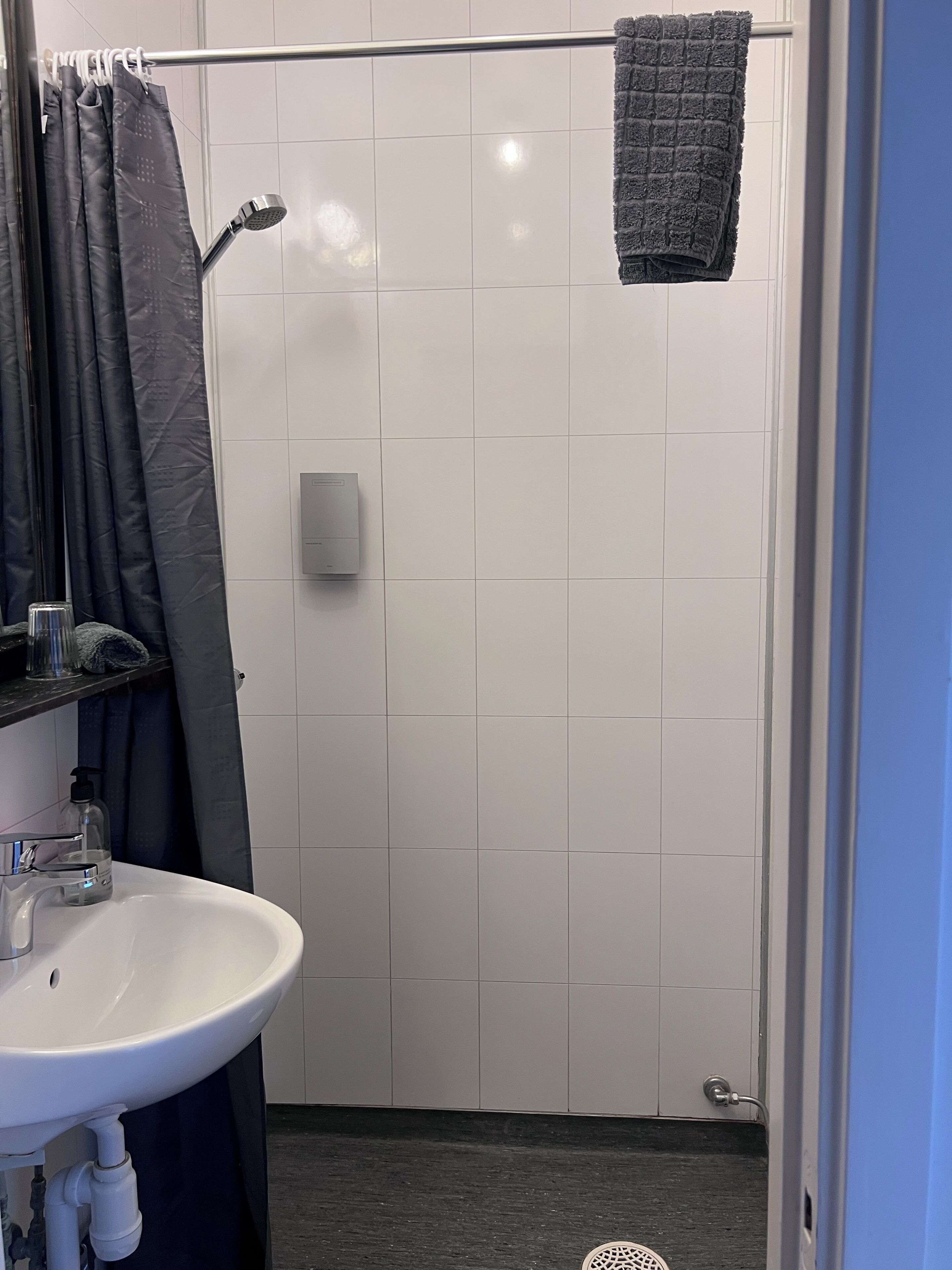 A bathroom with a white sink, a shower with a towel hanging, and a glass soap dispenser.