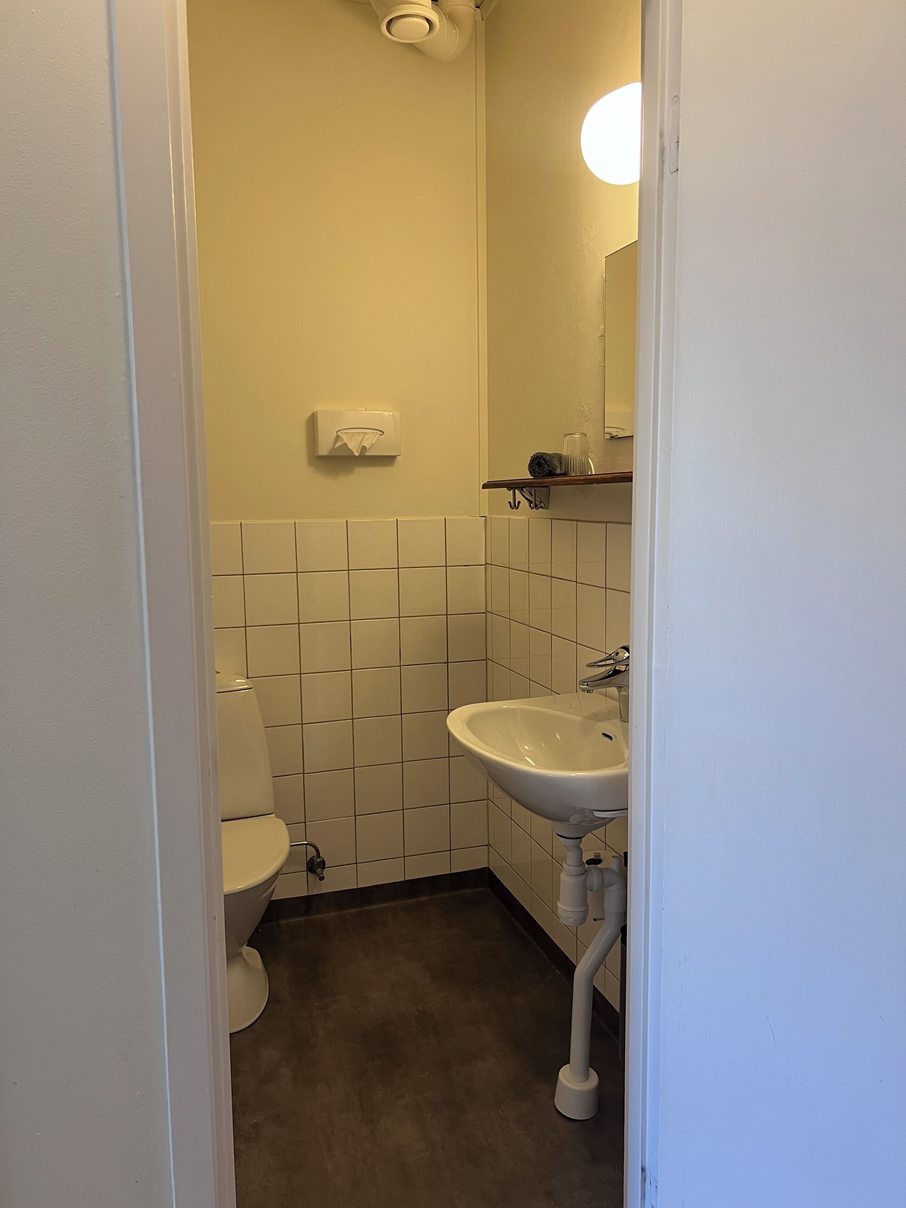 A small, clean bathroom with a toilet, sink, and a towel dispenser on the wall.