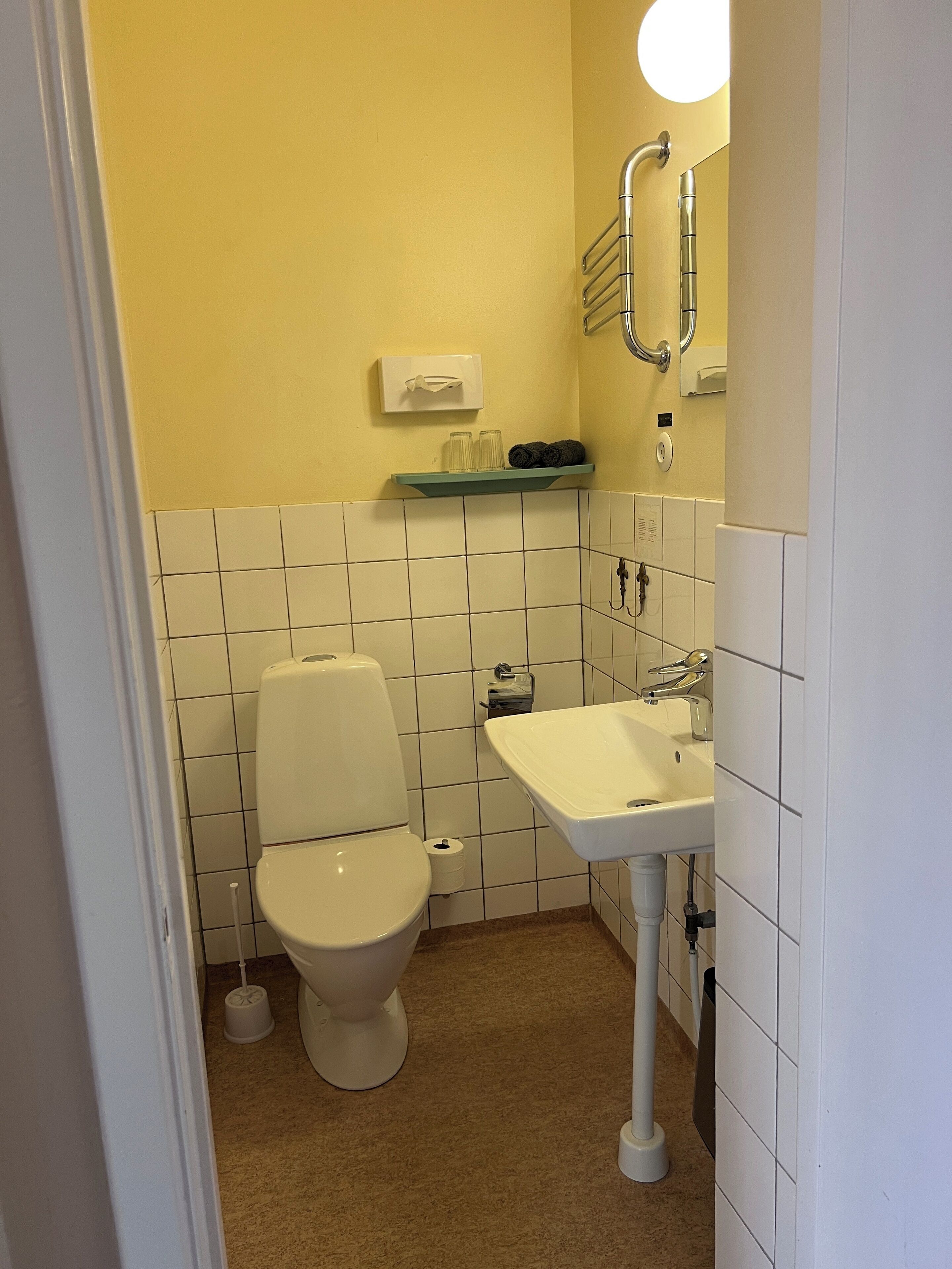 A small bathroom with a toilet, sink, and a shelf with toiletries.