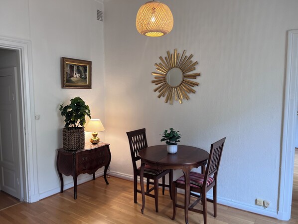Un comedor con una mesa y sillas de madera, una planta en maceta, una lámpara y un espejo decorativo en la pared.