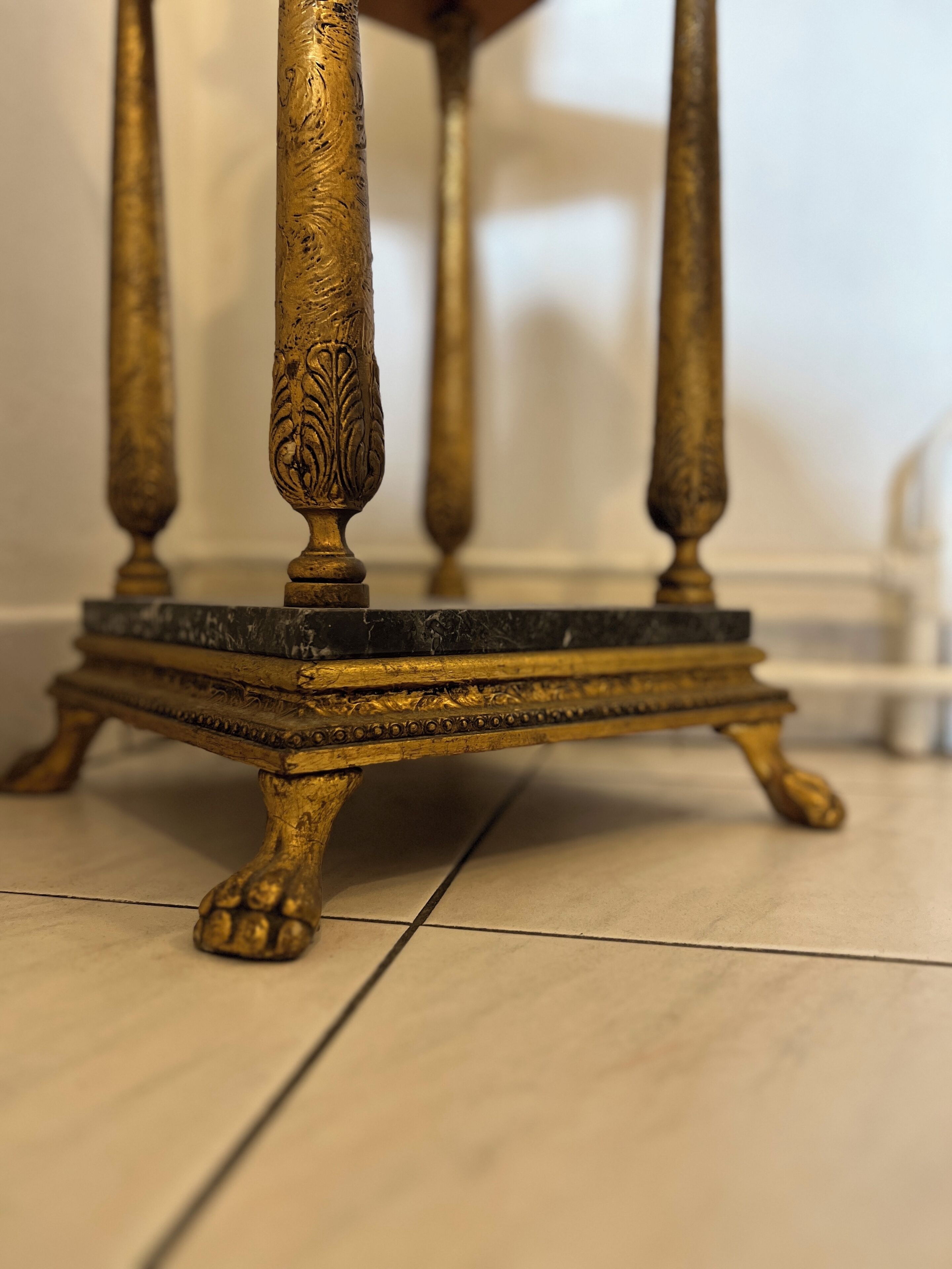 A close-up of a golden, intricately designed table leg with a marble base.