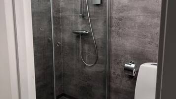 Une cabine de douche avec une porte en verre, une serviette accrochée au mur et des toilettes à côté.