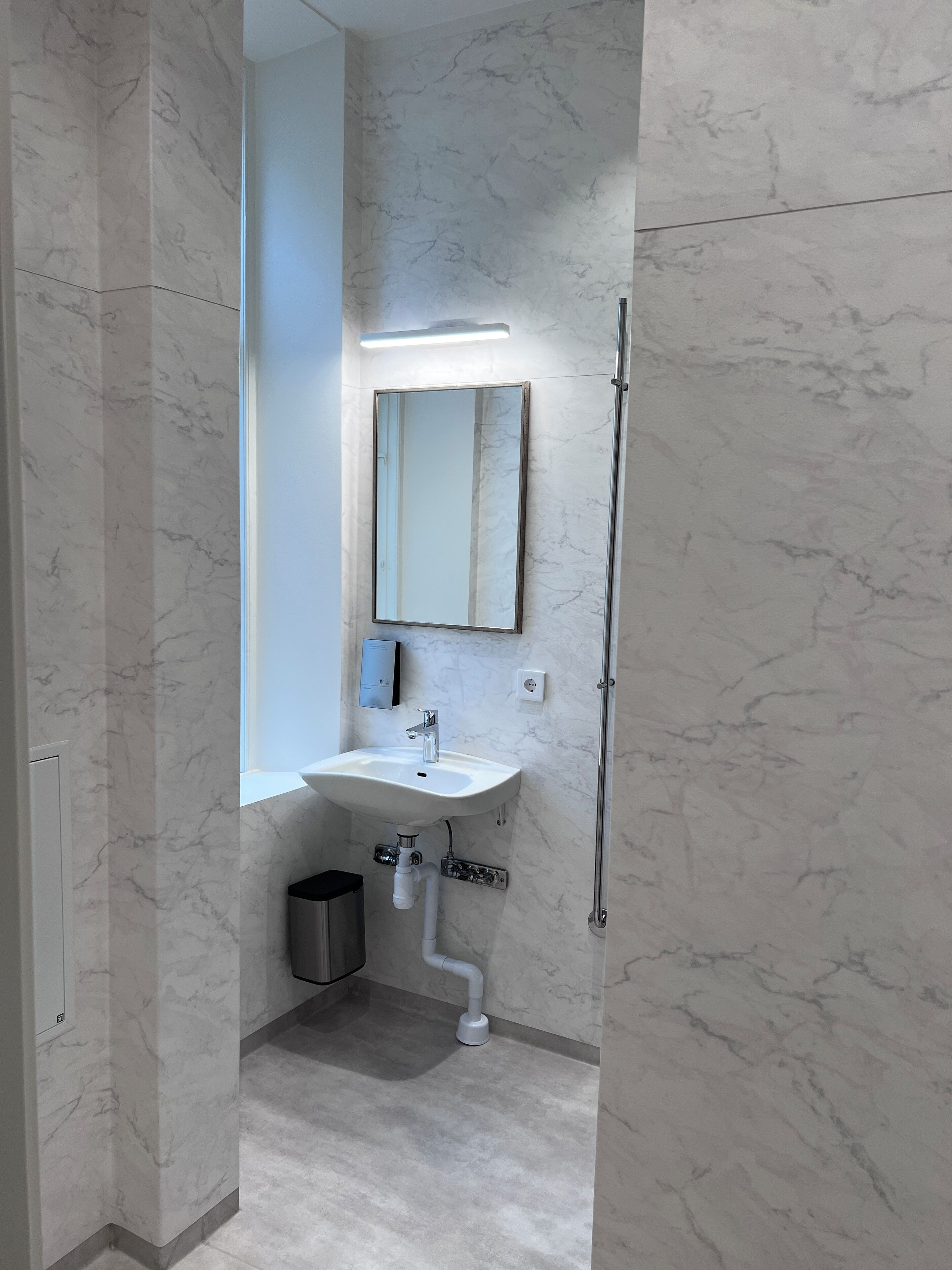 A bathroom with a white sink, mirror, and marble walls.