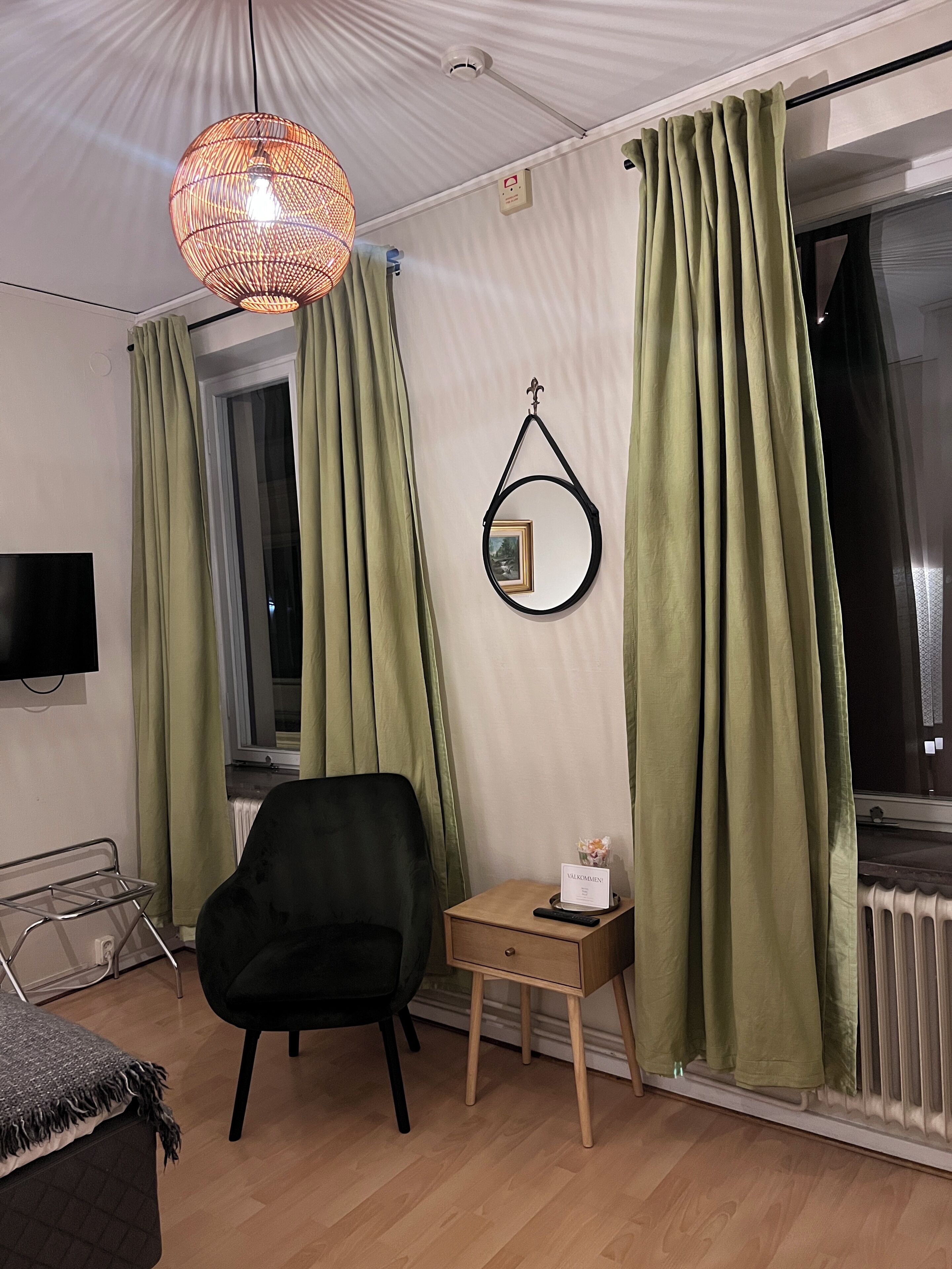 Habitación de hotel con una silla negra, una mesita de madera con un control remoto, un marco de fotos y una lámpara colgante.