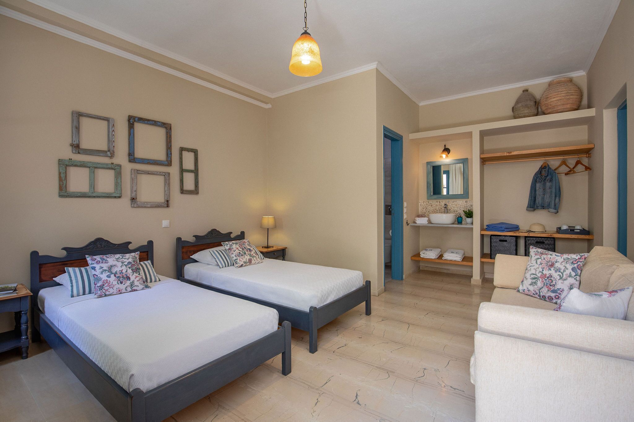 A bedroom with two beds, a sitting area with a sofa, and a small kitchenette.