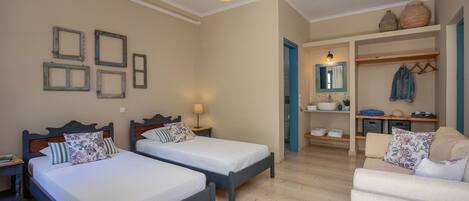 A bedroom with two beds, a sitting area with a sofa, and a small kitchenette.