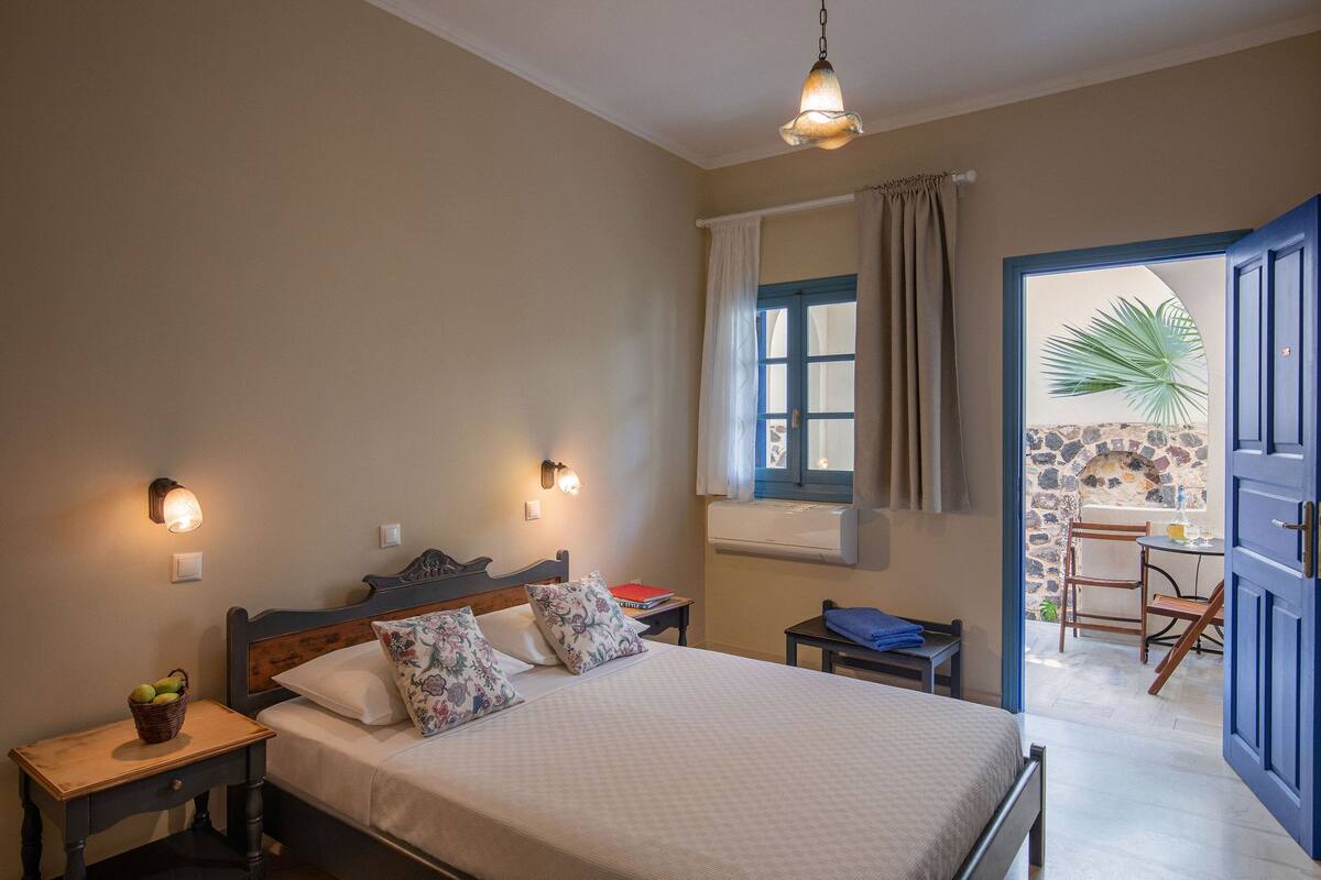 A bedroom with a bed, bedside tables, a window with curtains, a view of the outside, and a door leading to a balcony.