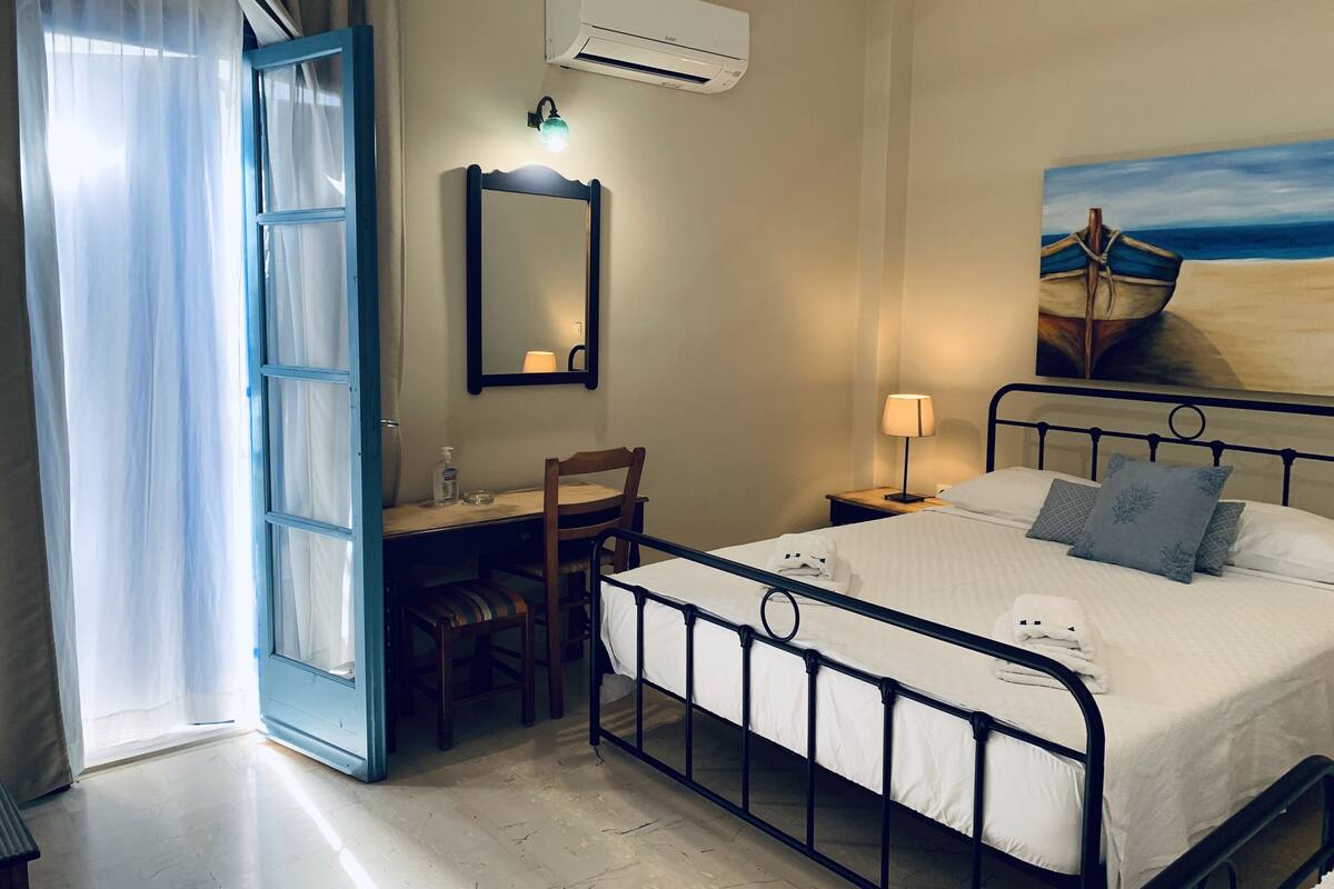 A hotel room with a bed, bedside table, lamp, desk with chair, and an air conditioning unit.