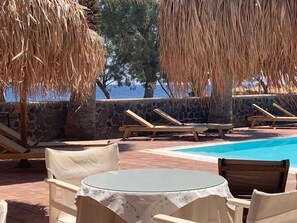 A poolside area with lounge chairs, a table, and a view of the sea. - The Boathouse Hotel (Santorini)