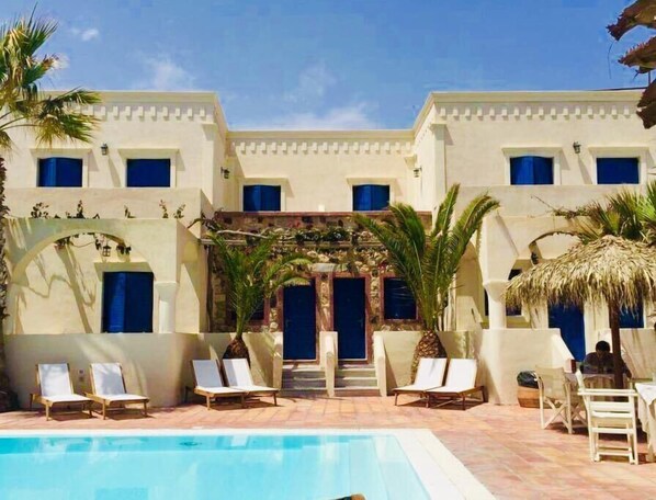 A poolside area with lounge chairs, a swimming pool, and a building with multiple windows and a stone facade.