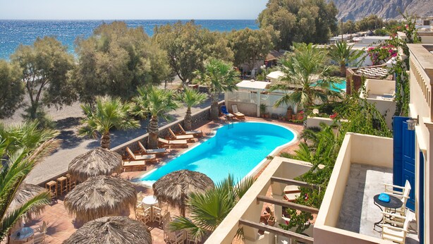 A pool area with lounge chairs and umbrellas, overlooking a beach and the sea. - The Boathouse Hotel (Santorini)